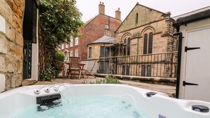 Un jacuzzi en un patio con edificios de piedra y una casa de ladrillo al fondo.