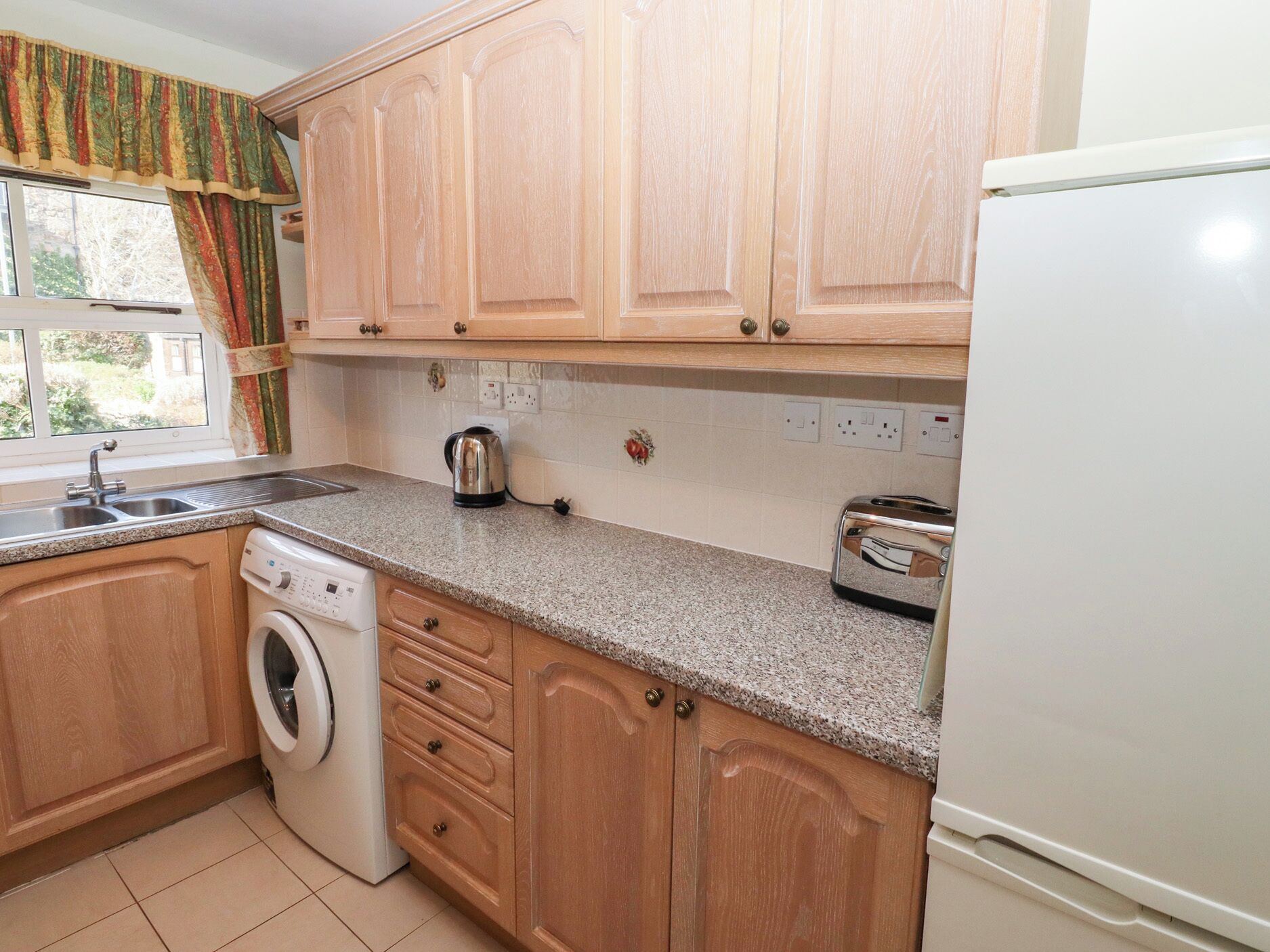 A kitchen with wooden cabinets, a washing machine, a toaster, and a refrigerator.