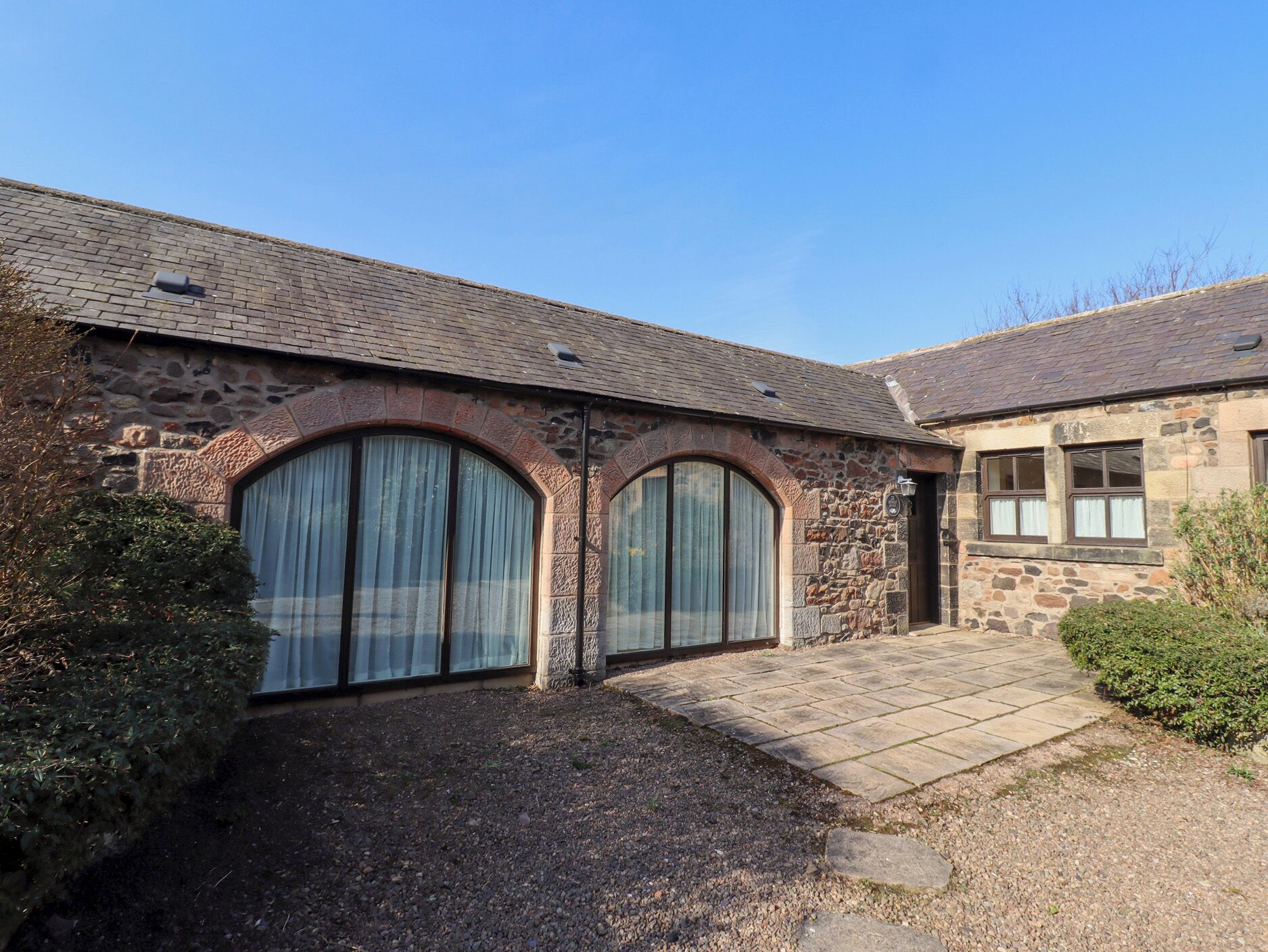 A stone building with two large arched windows and a gravel driveway.