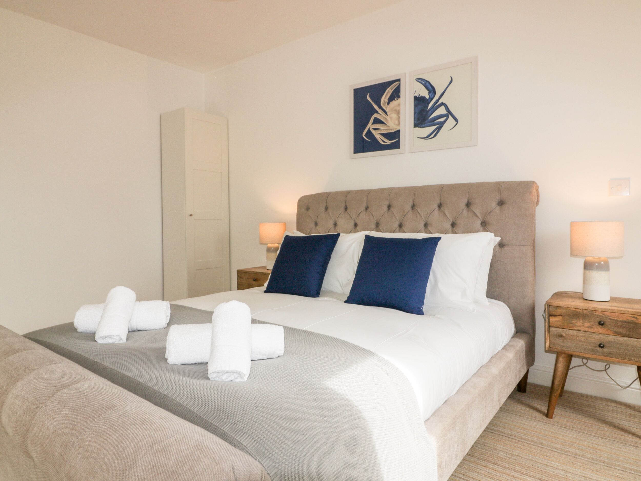 Una cama bien hecha con almohadas blancas y azules, un cabecero gris y dos cuadros en la pared encima.