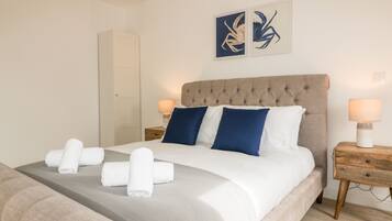 Una cama bien hecha con almohadas blancas y azules, un cabecero gris y dos cuadros en la pared encima.