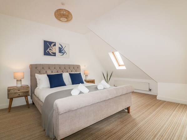 A bedroom with a large bed, two bedside tables, a ceiling light, a radiator, and a skylight.
