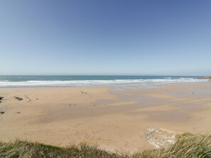 Uma extensa praia de areia com ondas suaves e céu claro.
