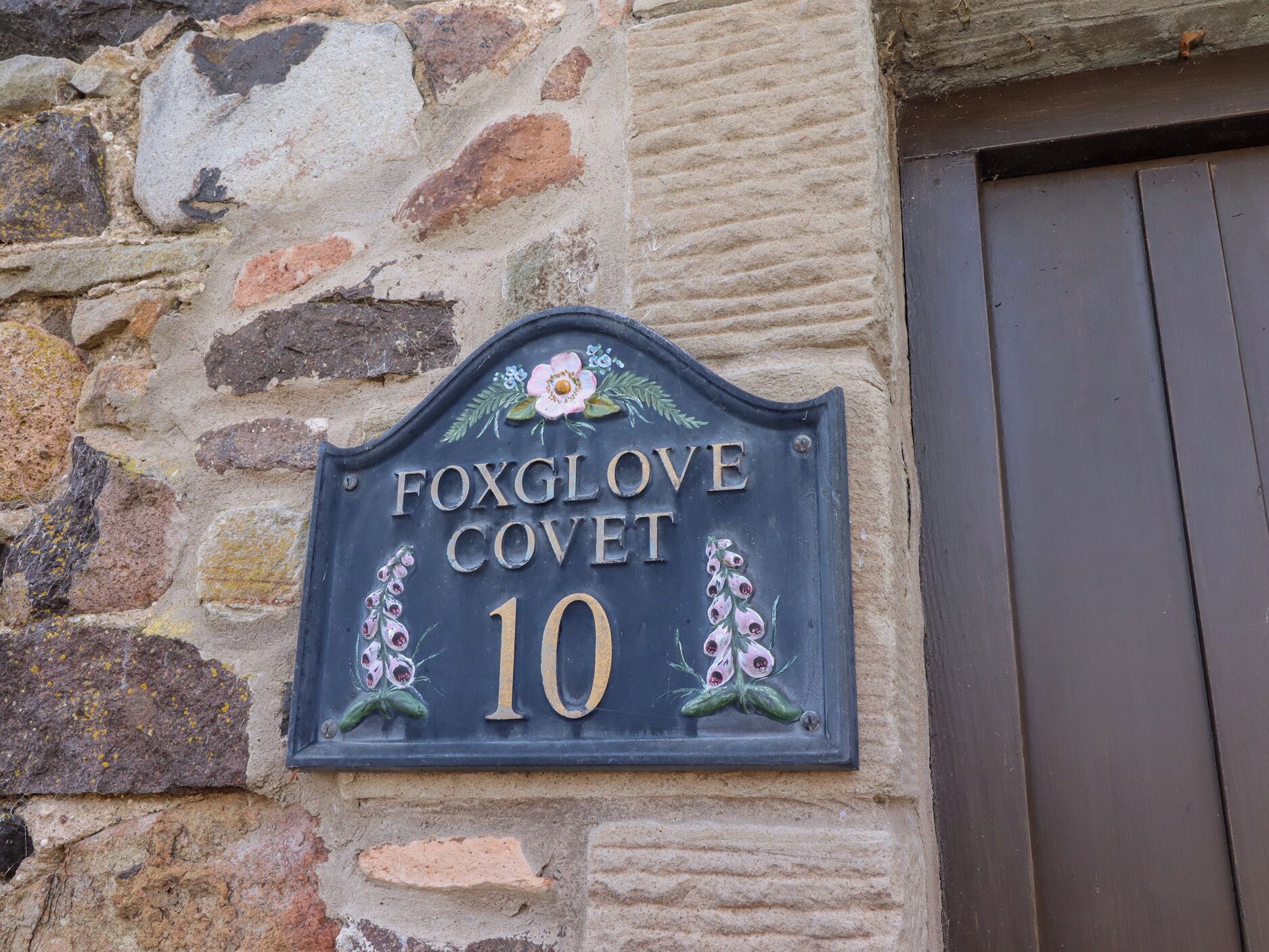 Talossa on kiviseinään kiinnitetty opaste, jossa lukee: «FOXGLOVE COVET 10».