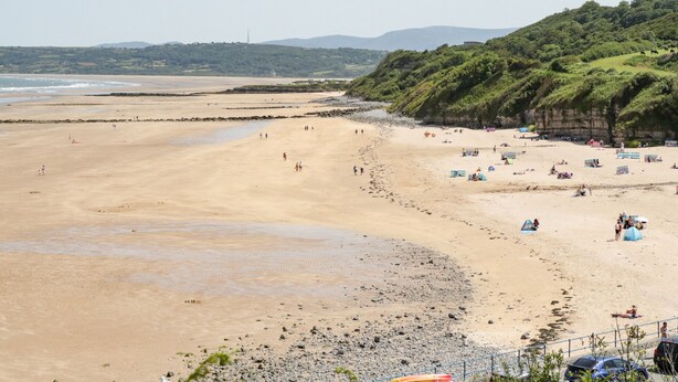 Ein weiter Sandstrand mit felsiger Küste, Zelten und Menschen.