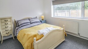Ein Schlafzimmer mit Bett, Nachttisch, Lampe, Kommode, Fenster und Heizkörper.