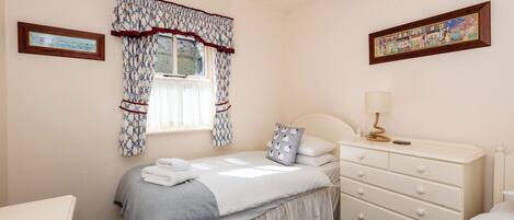 Un dormitorio con cama, mesita de noche, lámpara y dos cuadros en la pared.
