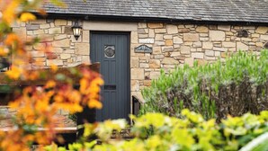 A stone cottage with a dark door, a sign reading '18 Blueberry Cottage,' and a lantern above the door. - Blueberry Cottage (Wooler)