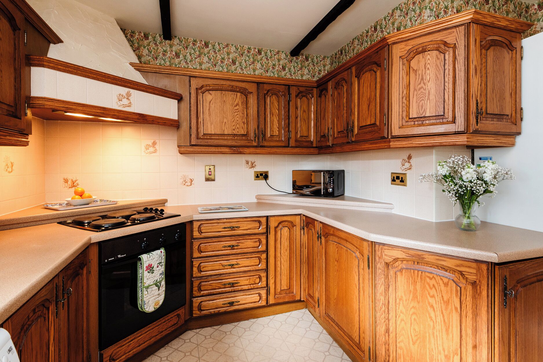 A kitchen with wooden cabinets, a stove, a microwave, and a vase with flowers.