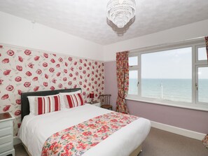A bedroom with a bed, a nightstand, a chair, a window with a view of the sea, and a chandelier.