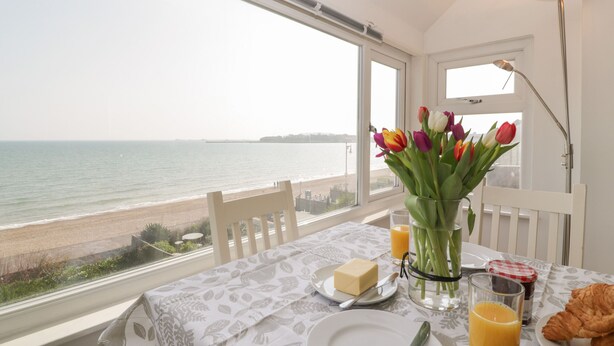 Une table à manger avec vue sur la mer, un vase de tulipes et des aliments pour le petit-déjeuner.