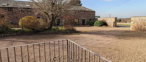 A stone building with a gravel courtyard, a metal railing, and a tree.