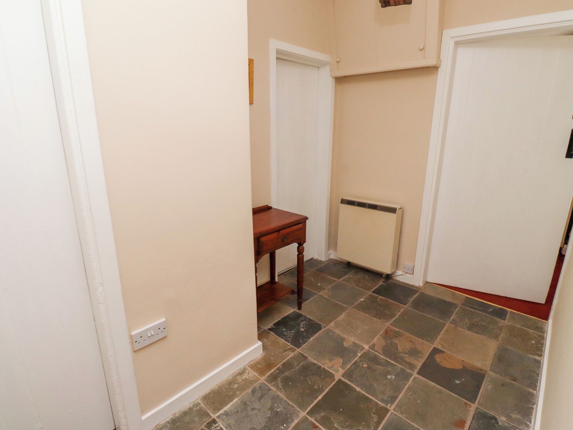Un couloir étroit avec un sol carrelé, une table en bois et un radiateur.