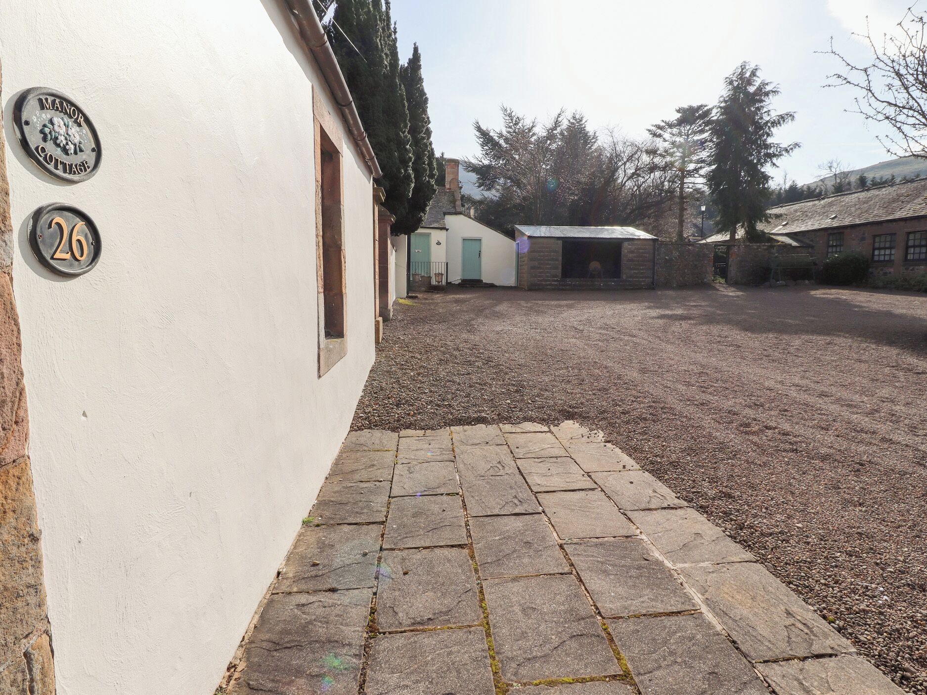 En innergård med en grusgång, en vit byggnad med ett nummer på fasaden och en liten byggnad i bakgrunden.