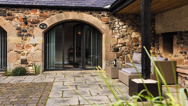 A stone building with a tiled roof, a glass door entrance, and outdoor seating.