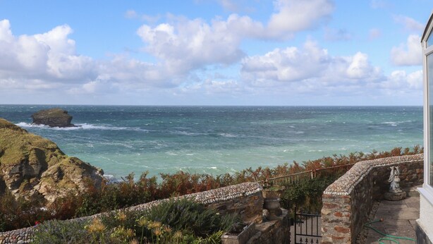 A coastal view with a rocky cliff, a stone wall, and a statue. - Beach Cottage (Redruth)