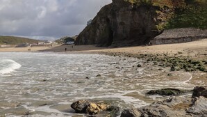 A coastal scene with a rocky beach, a cliff with a building on top, and a view of the sea. - Beach Cottage (Redruth)