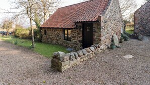 A stone cottage with a red-tiled roof, a wooden door, and a gravel driveway. - Tile Rouge (Wooler)