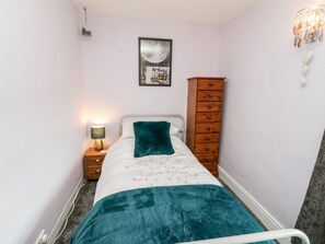 A bedroom with a bed, a nightstand with a lamp, a wooden dresser, and a wall-mounted picture. - The Lodge (Whitby)