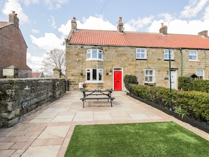 A stone building with a red door, a picnic table, and a well-maintained lawn. - The Lodge (Whitby)