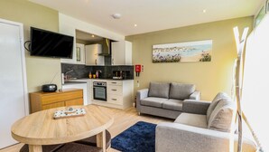 A compact living space with a kitchenette, a sofa, a dining table, and a TV mounted on the wall. - Chalet 126a (Cromer)