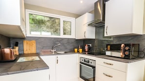 A modern kitchen with white cabinets, a stainless steel range hood, a built-in oven, and a microwave. - Chalet 126a (Cromer)