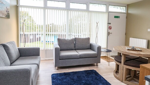 A modern living room with grey sofas, a blue rug, and a wooden table. - Chalet 126a (Cromer)