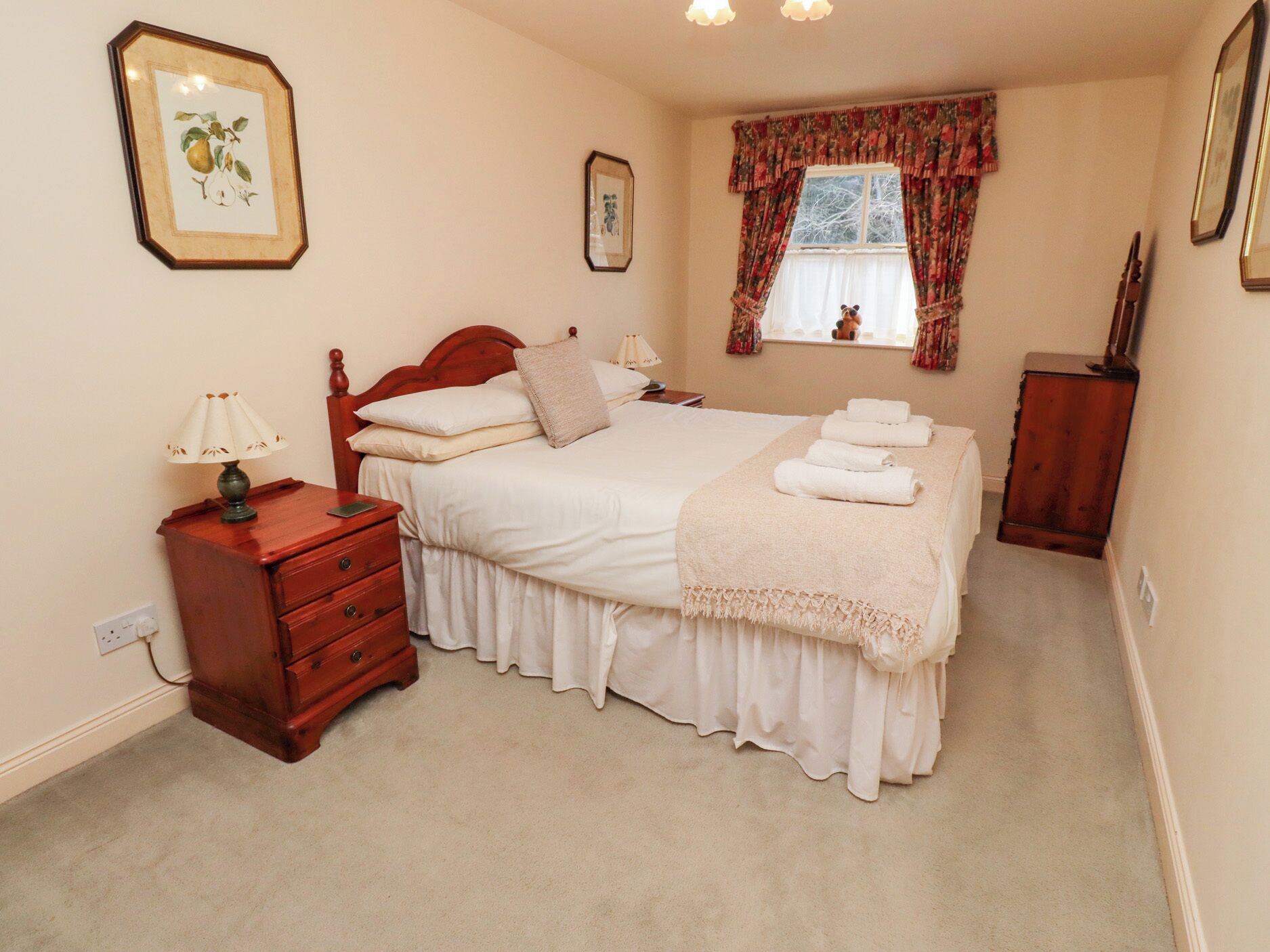 Un dormitorio con una cama grande, mesitas de noche, un aparador y una ventana con cortinas.