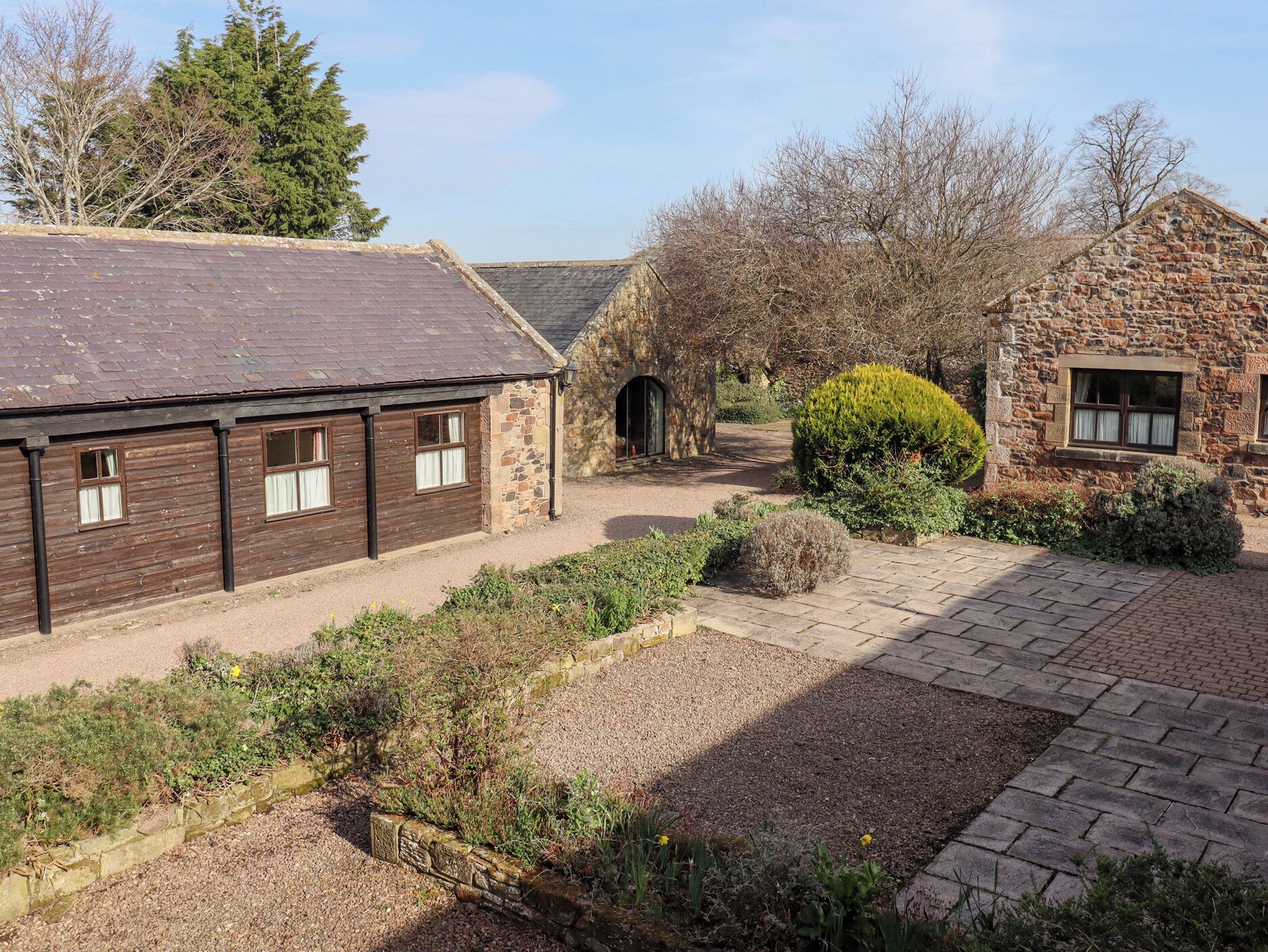 A traditional stone building with a gravel courtyard and a wooden structure with windows.