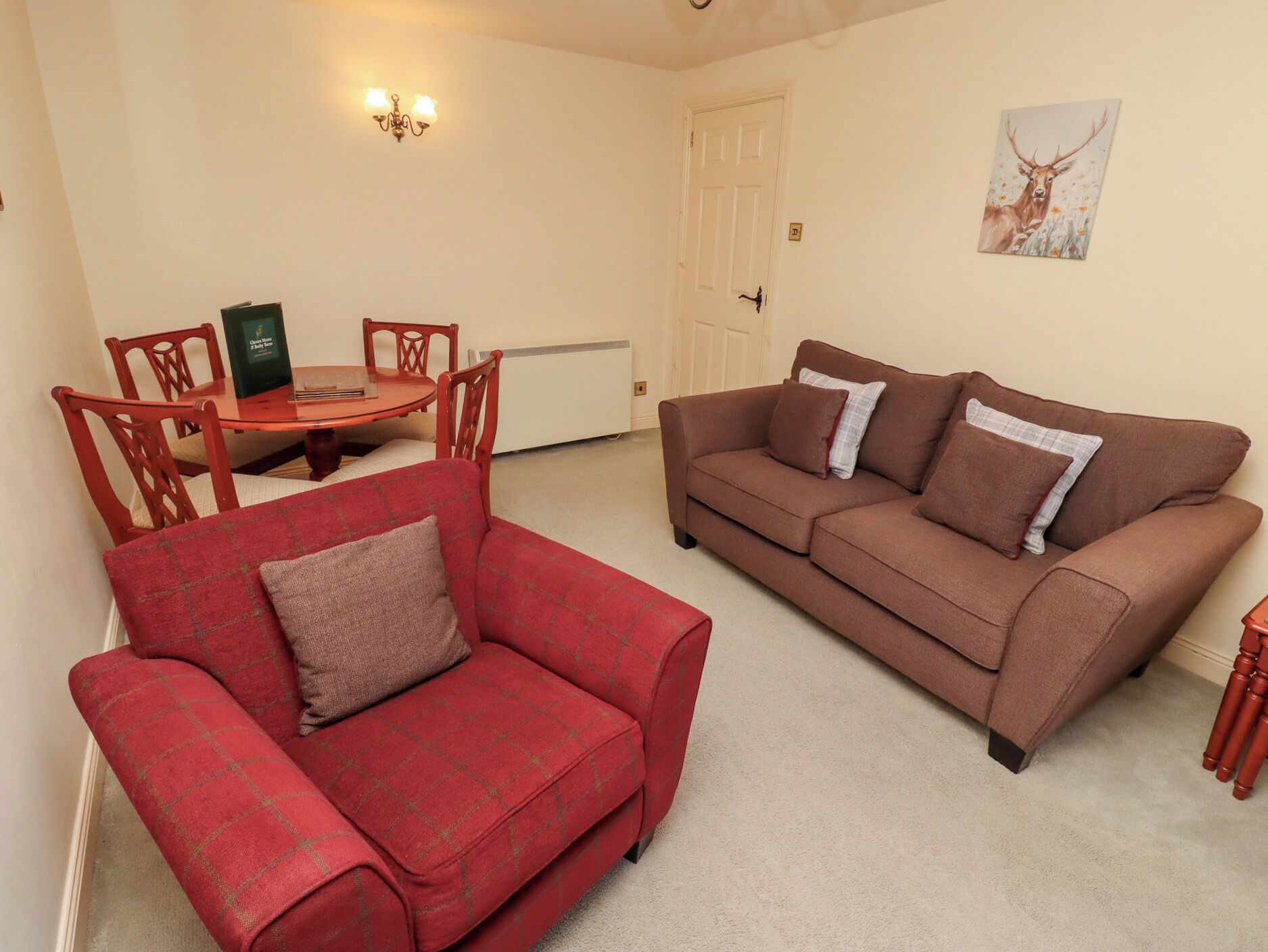 A living room with a red sofa, a brown sofa, a dining table with chairs, a wall-mounted light fixture, and a door.
