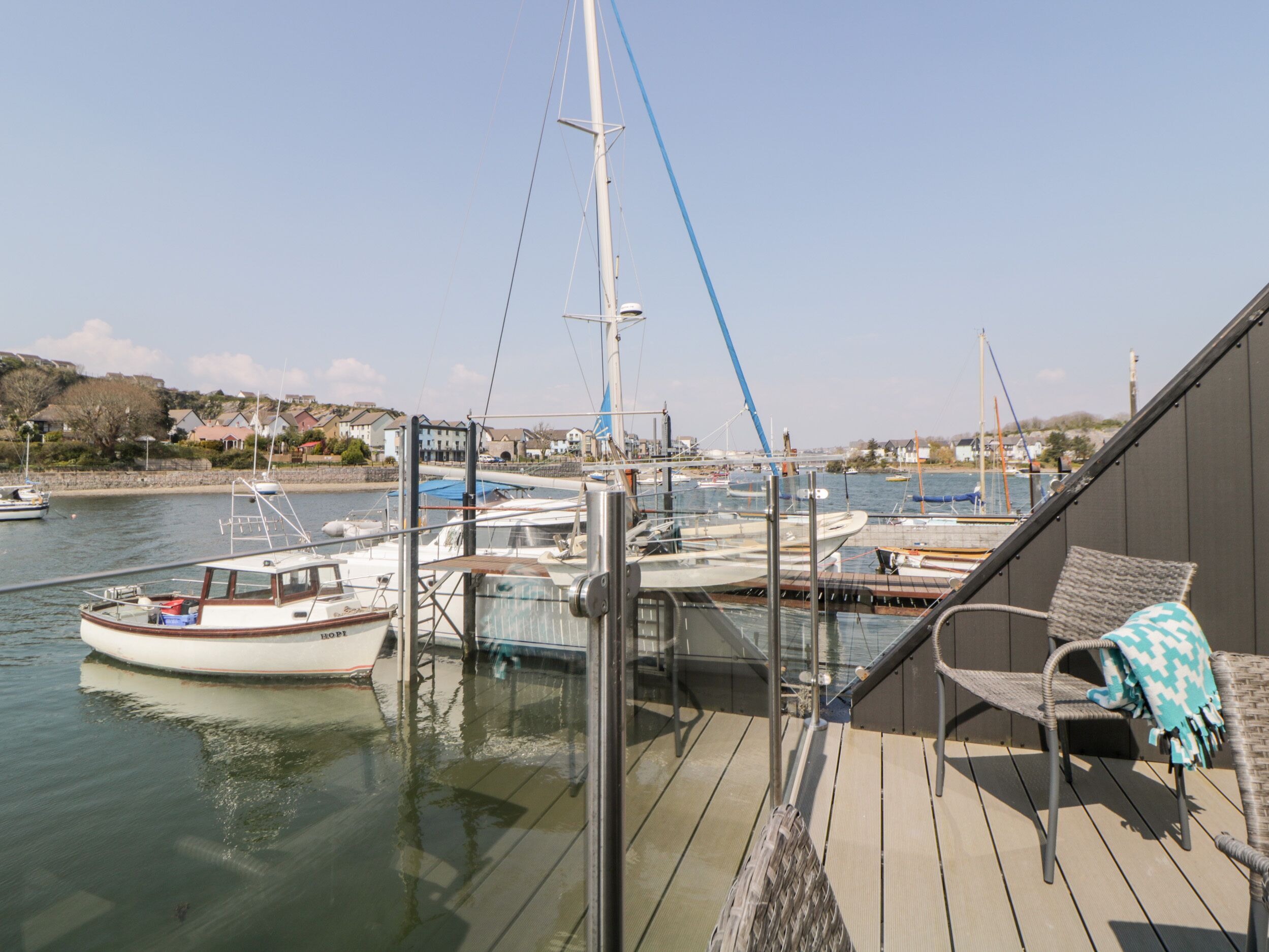 A deck with a view of a marina, including boats and houses in the background.