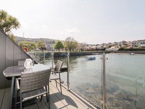 A balcony with a table and chairs overlooking a river, with houses in the background.