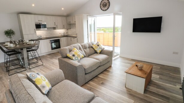 A modern living room with a grey sofa, a coffee table, and a TV mounted on the wall. - Caban Y Mor (Narberth)