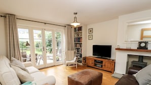 Een woonkamer met een bank, voetenbankje, salontafel, televisie, boekenkast en een open haard.