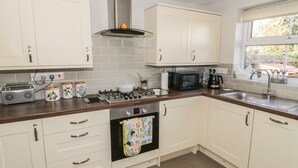 A modern kitchen with white cabinets, a gas stove, a microwave, and a window with a view of greenery.