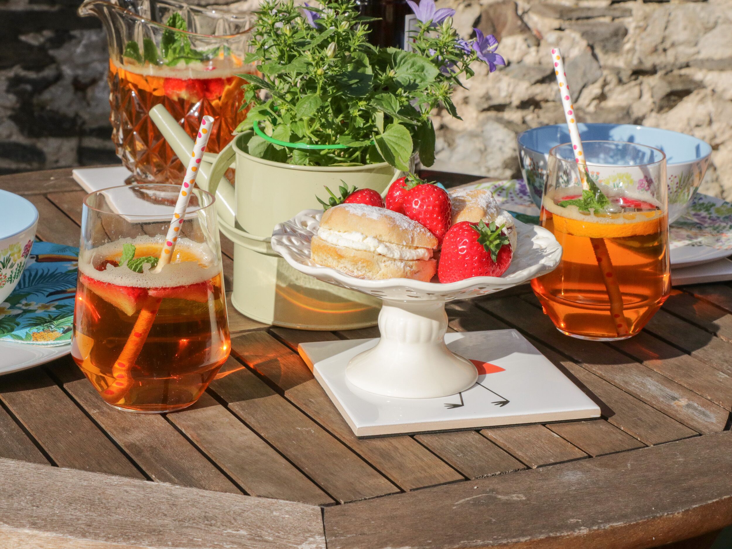 A wooden table with a pitcher, a bowl of strawberries, and two glasses of tea.