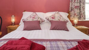 A bedroom with a bed, two nightstands, a lamp, a chair, and a window with curtains. - Mount Pleasant Cottage (Grange-over-Sands)
