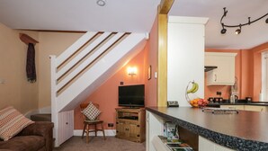 A cozy living room with a brown sofa, a wooden chair, a TV, and a bookshelf. - Mount Pleasant Cottage (Grange-over-Sands)