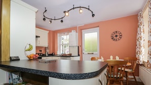 A kitchen with a central island, white cabinets, a fruit basket, and a clock on the wall. - Mount Pleasant Cottage (Grange-over-Sands)