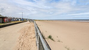 Une promenade en bord de mer, bordée de cabanes de plage et donnant sur une plage de sable.