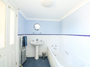 A bathroom with a white sink, a round mirror, a bathtub, and a towel rack. - The Hemploe (Mablethorpe)