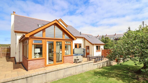 A modern house with a large glass door, a patio with outdoor furniture, and a well-maintained lawn.