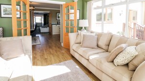 A spacious living room with a large beige sofa, a wooden coffee table, and a view through open French doors to a balcony.