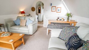 A cozy living room with a sofa, a coffee table, and a dining area with a table and chairs. - 19 Honicombe Park (Gunnislake)