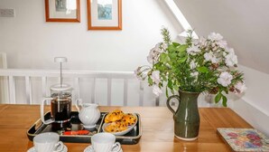 A breakfast setup with a coffee maker, teapot, pastries, and a floral arrangement on a wooden table. - 19 Honicombe Park (Gunnislake)