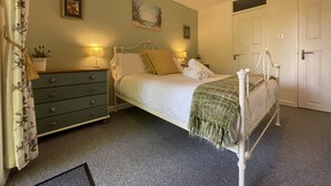 A neatly arranged bedroom with a bed, bedside lamps, a dresser, and a door. - 19 Honicombe Park (Gunnislake)