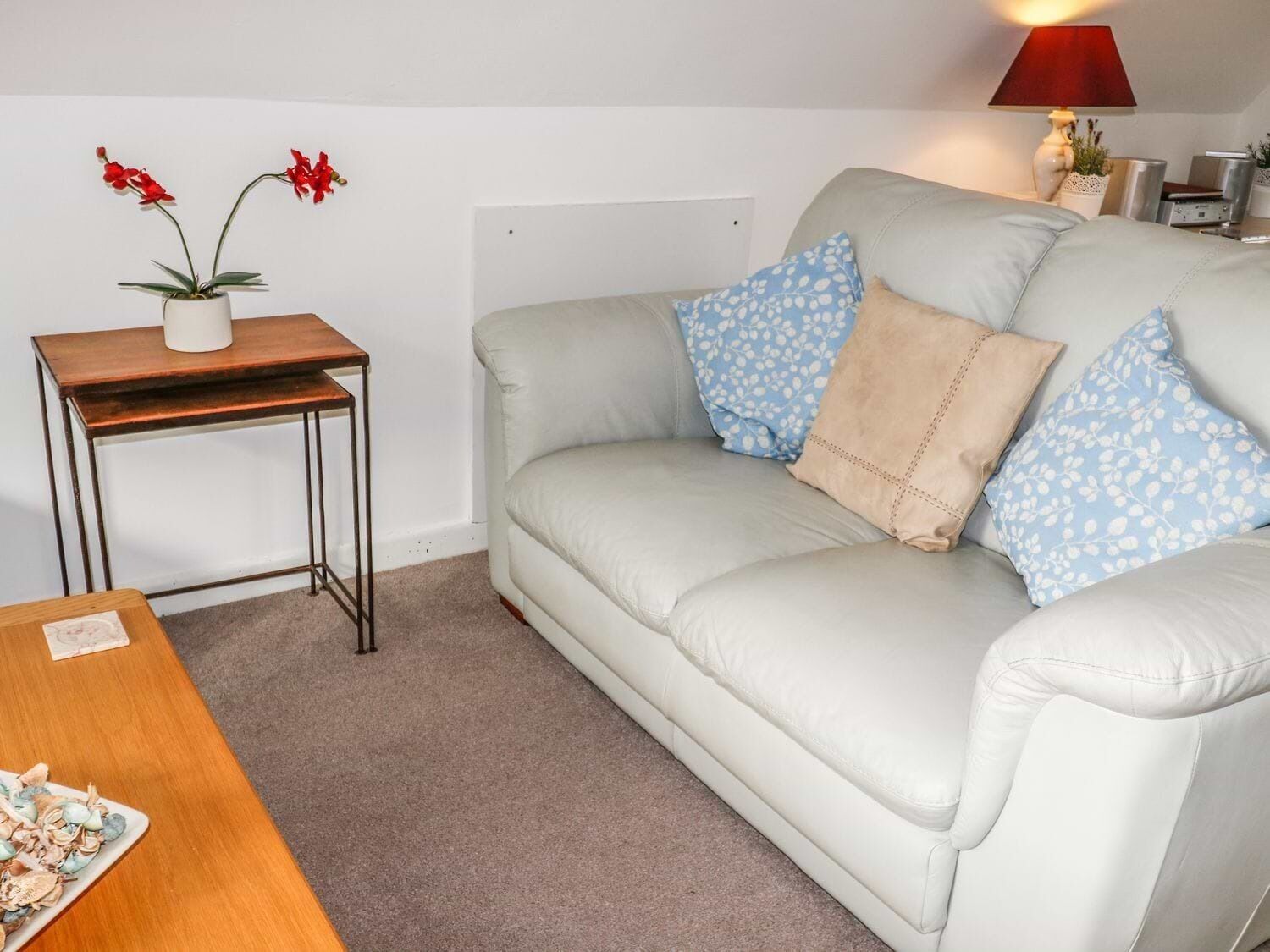 A living room with a light grey sofa, two blue patterned pillows, a wooden side table with a potted plant, and a small table with a plate of food.