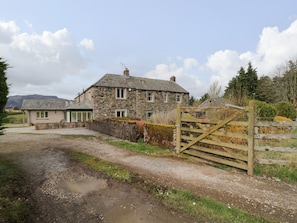 A stone house with a gravel driveway and a wooden gate.