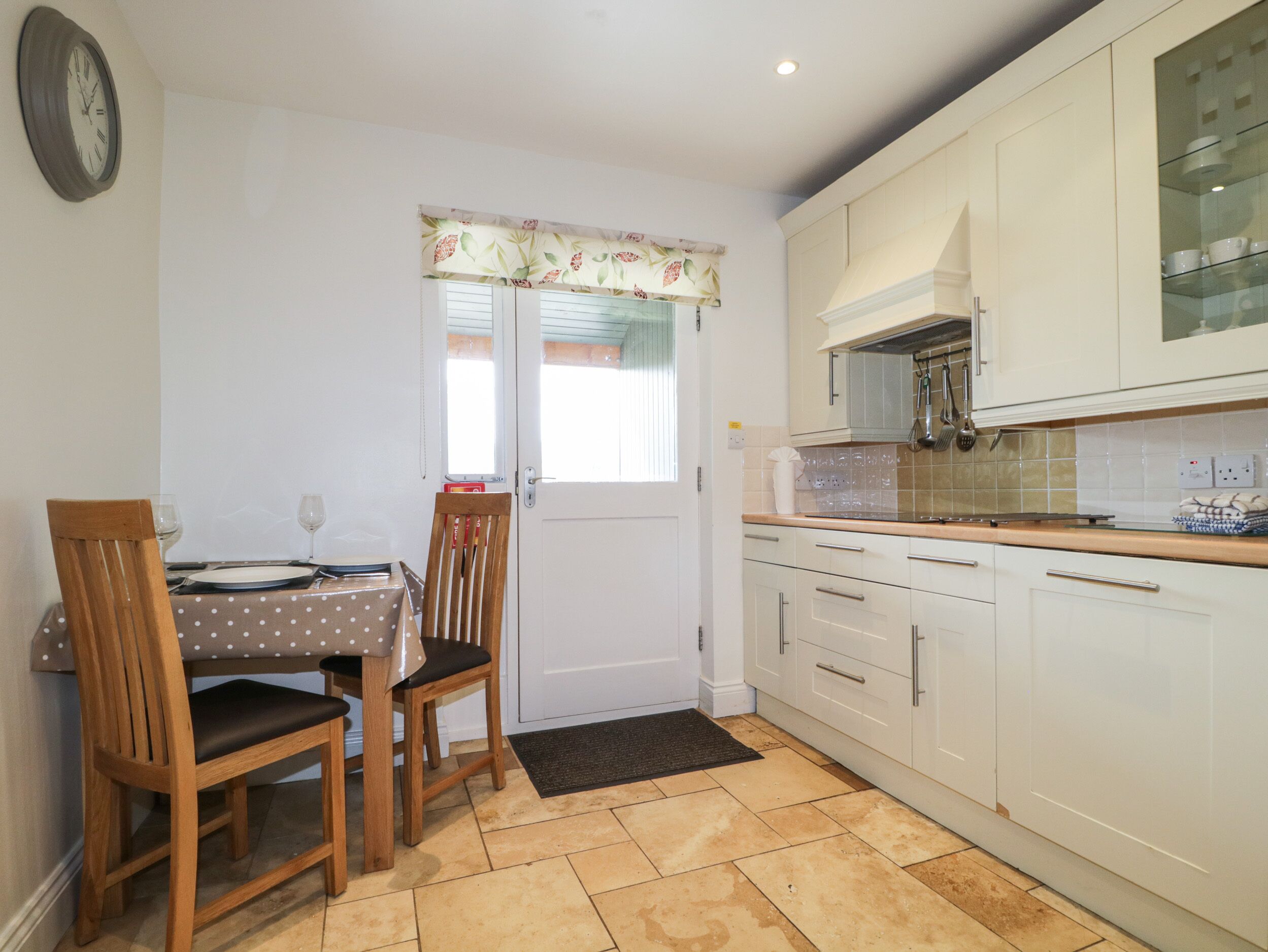 A compact kitchen with white cabinets, a dining table with two chairs, and a clock on the wall.