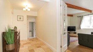 A spacious living area with a wooden floor, a television, and a sofa. - Glen Cottage (Penrith)